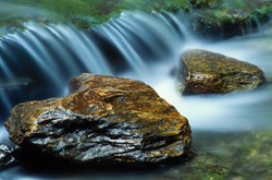 A pair of river rocks with a small waterfall flowing behind them