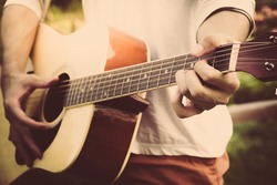 Closeup of young man's hands playing acoustic guitar at the park. - Vintage filter.