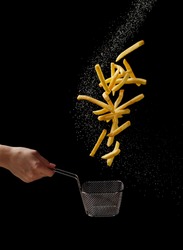 French fries - fried potatoes flying out of basket in hand, fly fastfood isolated on black background