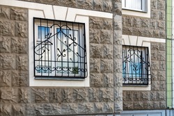 Wrought iron patterned grilles are installed outside on the first floor windows of the apartment building for safety.