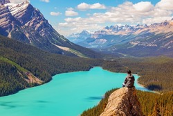 A hiker sits on the peak of Bow Summit with stunning view of Peyto Lake in the Canadian Rockies of Banff. The glacier-fed lake is famous for its bright turquoise colored waters in the summer.