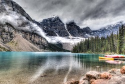 Moraine Lake with clouds descending on the Valley of the Ten Peaks in the background and some canoes on the lake. HDR rendering.