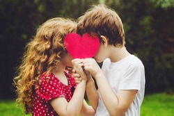 Cute children holding red heart shape in summer park. Valentines day background.
