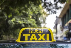 taxi cab sign of taxi in Delhi with city background, India. NCR is short name, full name is National Capital Region. It's mean area around Delhi such as Gurgaon