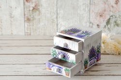 A handmade chest of trinket drawers decoupaged with vintage paper with pots of Lavender on a rustic wooden background