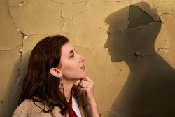 Beautiful througtful young woman thinks of her ideal boyfriend man or lover represented by a shadow on the wall.