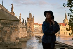 Focus on background. Prague Silhouette. Stylish young woman wearing black hat with Charles Bridge on background. Elegant retro lady fine art portrait.