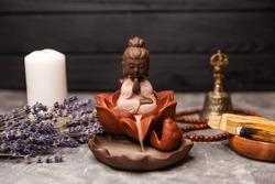 Buddha statue in the smoke of incense on black. Candle incense. Calming zen interiors with buddha statue. Buddha meditation. Aromatherapy, spa table setting with buddha. Lighting perfumed candles.