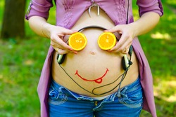 On the belly of a pregnant woman smiley face baby and headphones. The child listens to the music in the womb