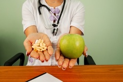 Health, choice between natural product and synthetic medicine. Doctor in medical gown offering alternatives fresh apple or pharmaceutical pills. Doctor holding apple or dietary food supplement pills.