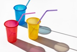 Three multi-colored plastic cups with straws on a white background. Long shadows, studio shot.