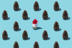 Christmas pattern from pine cones on a blue background. Red Santa hat on a silver ball.