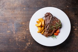 T-Bone Steak with roasted potato wedges on white plate on wooden background