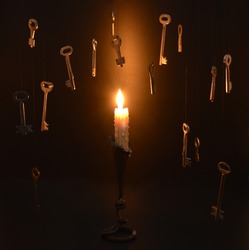 Single burning candle in candlestick with hanging metal keys