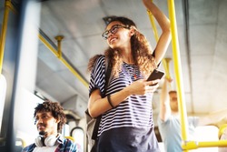 Young adorable joyful woman is standing on the bus using the phone and smiling.