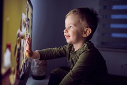 A bedtime ritual for toddlers. The boy touched the TV screen with one hand. A close-up shot of a kid in pajamas sitting right in front of the TV and staring at a cartoon Watching favorite cartoon show