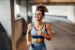 A happy fit runner is running under the underpass with a smile on her face with minimum effort. Healthy habits-healthy body. An urban runner running on the road.