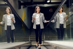 A happy businesswoman is ascending the escalator and going to her office. An elegant young woman going to work. A woman climbing up the escalator and exiting an underground garage.