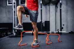 Exercises with hurdles. Close-up shot of a man’s legs in sportswear that skips small hurdles. Jumping over obstacles and warming up for training. Healthy lifestyle, strong movement, dynamism