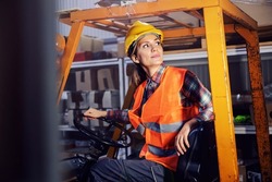 A female storage worker driving freight on forklift.