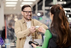 A smiling man giving credit card to a cashier and paying for groceries in supermarket.