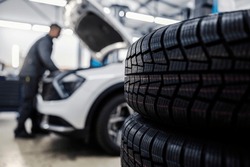 Close up of a new tires in foreground with worker fixing car in blurry background at mechanic's shop.