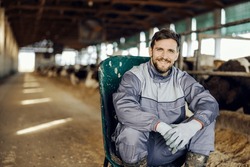 Portrait of a farmer sitting on chair in barn and smiling at the camera. Livestock and agriculture concept.