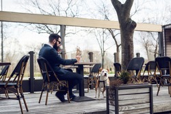 Businessman checking email and drinking coffee at cafe bar with his dog.