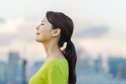 Young asian woman closing eyes in front of the city.