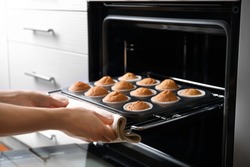Woman taking baking tray with cupcakes from oven