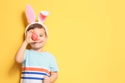 Cute little boy with bunny ears holding Easter egg on color background