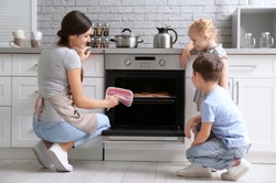 Little kids watching their mother bake cookies in oven indoors