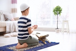Muslim boy praying on rug at home