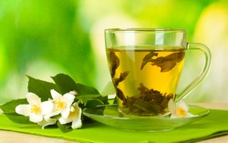 cup of green tea with jasmine flowers on wooden table on green background