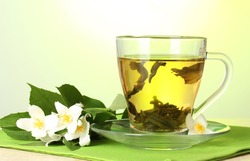 cup of green tea with jasmine flowers on wooden table on green background