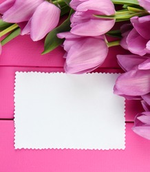 Beautiful bouquet of purple tulips and blank card on pink wooden background