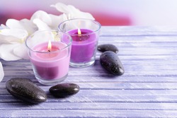 Beautiful colorful candles, spa stones and  orchid flower,on color wooden table, on light background