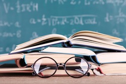 Books and glasses on wooden table on blackboard background