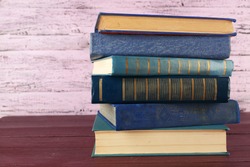 Stack of books on wooden table on pink wooden wall background