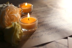 Beautiful rose with candles on music sheets, closeup
