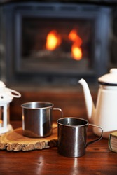 Teapot and mugs on vintage wooden table. Fireplace as background