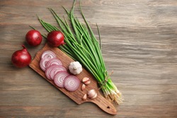 Red onions circles, green onion with garlic on board against wooden background