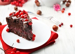 Piece of chocolate cake with cranberries on plate with nuts on wooden table, closeup