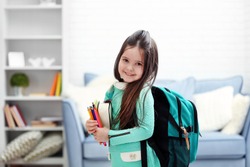 Little girl with green back pack holding stationery in living room