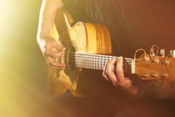 Young man playing on acoustic guitar on dark background with light effect