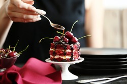 Female hand decorating cherry cake on stand