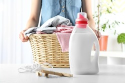 Woman holding wicker basket with clothes and detergent on table