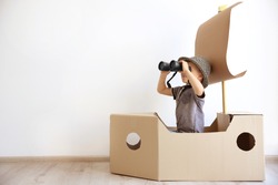 Little boy playing with cardboard ship on white wall background