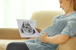 Pregnant woman with baby ultrasound scan sitting on couch at home