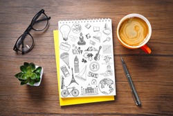 Notebook with drawings and cup of coffee on wooden table. Creative concept.